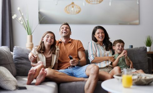 How Much House Do You Need? Cheerful parents and their kids having fun while watching a movie on sofa in the living room.